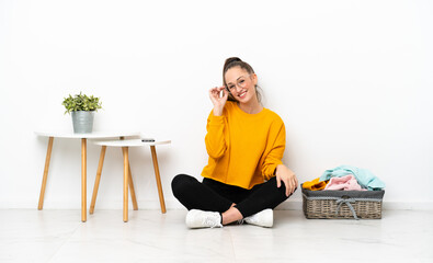 Young caucasian woman folding clothes sitting on the floor isolated on white background with...