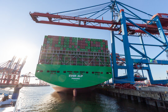 Rear view of the massive container ship Ever Alp docked at Terminal Burchardkai with huge cranes and sun flare