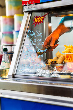 Hand with tongs reaching to pick up takeaway jam donut food at sideshow stall at event