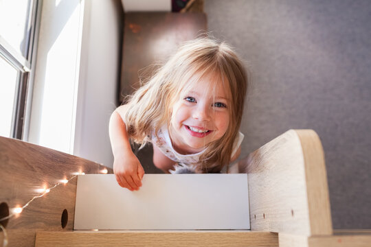 Happy little Australian girl with messy hair climbing up bunk bed ladder in her bedroom