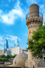 Vertical view of the Shirvanshah Palace Mosque in Baku Azerbaijan with domes and minaret framed by modern skyscrapers under a bright blue sky.