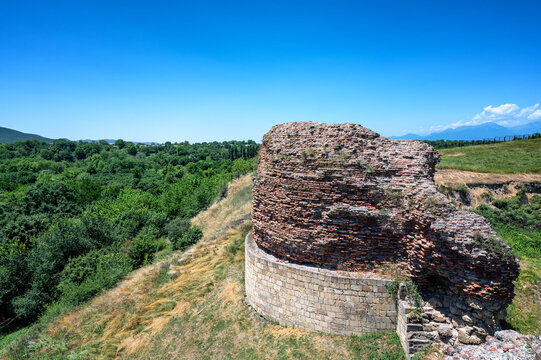 Ancient brick and stone city walls in Gabala, Azerbaijan, overlooking green hills and forest under a bright summer sky.