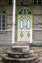 A carved wooden entrance door of the Agolu Mosque in Lahij, Azerbaijan, framed by stone architecture in a mountain village setting.