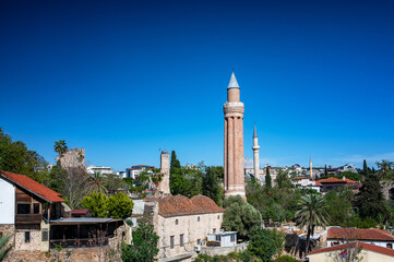 Panoramic view of Antalya, Turkey, showing the Yivli Minaret Mosque and clock tower surrounded by Old Town rooftops under a clear blue sky.