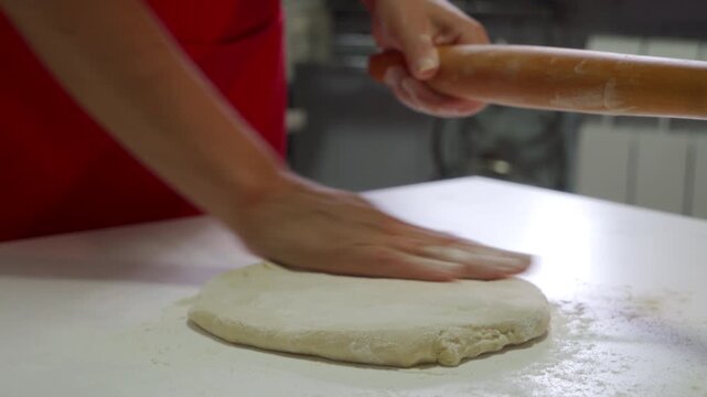 Soft white dough sits on a floured surface. A wooden rolling pin moves swiftly in the cook's hands as they flatten the raw pastry for baking.