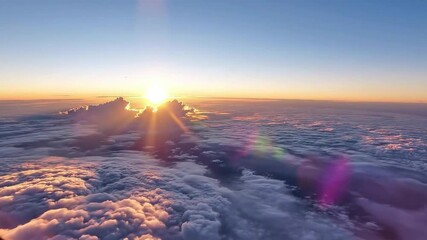 An aerial view of the sun on the horizon casting brilliant golden rays over an endless sea of white and grey clouds under a clear blue and orange sky