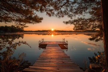 Naklejka premium Scenic sunrise over a calm lake, with a wooden dock and framing trees