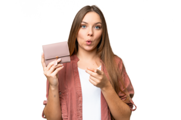 Young blonde woman holding a wallet over isolated chroma key background surprised and pointing front