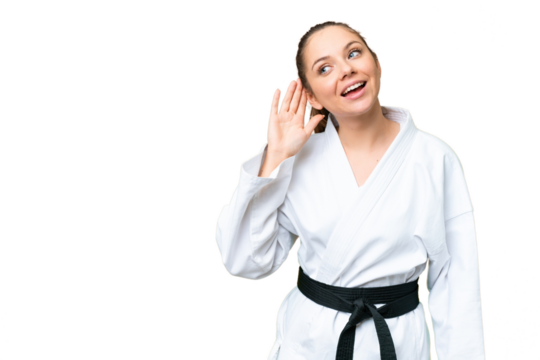 Young blonde woman doing karate over isolated chroma key background listening to something by putting hand on the ear