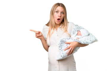 Young pretty pregnant woman with her newborn baby over isolated chroma key background surprised and pointing side