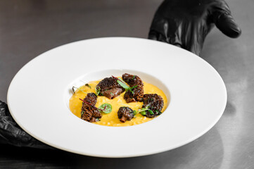 Gourmet braised beef cheek, morel mushroom and saffron risotto dish served by a chef in black gloves.
