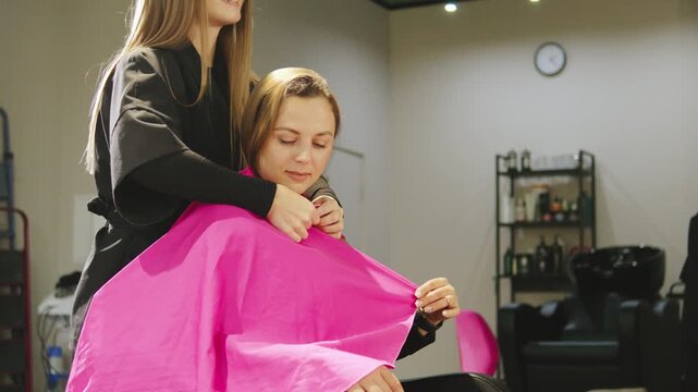 Hair stylist prepares client for haircut in a modern salon with bright lighting and stylish decor