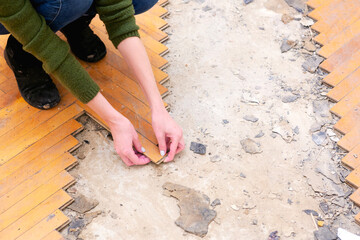 A woman carefully dismantles wooden parquet.