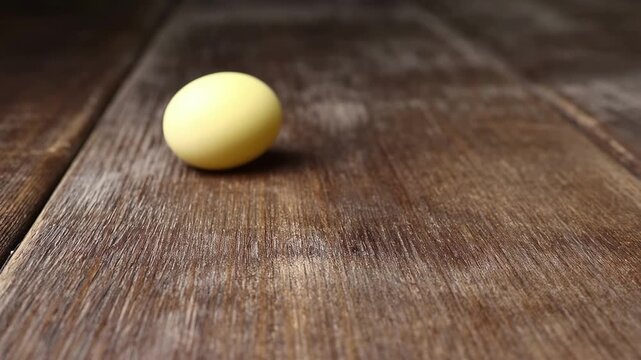 Pastel yellow egg rolling on rustic wooden table, showcasing texture contrast and natural lighting, video footage