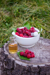Fresh raspberries in a mortar with a bottle of natural herbal extract or essential oil outdoors.