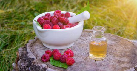 Fresh raspberries in a mortar with a bottle of natural herbal extract or essential oil outdoors.