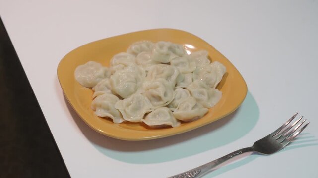 Hot meat dumplings fill the yellow square plate on the white table. A silver fork lies nearby as the fresh savory meal steams, ready to be enjoyed for dinner.