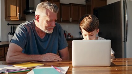 Helping grandson use laptop computer. Grandfather guides boy over homework. They sit at kitchen table. Family learning and tutor support. Natural sunlight fills kitchen interior. Calm study at table. - Powered by Adobe
