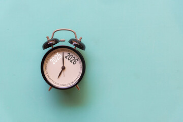 Obraz premium 2025 and 2026 on black alarm clock on blue background, Merry Christmas and Happy new year concept. Copy space and banner for text