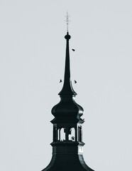 Sylwetka zabytkowej wieży kościelnej z krzyżem i ptakami na tle nieba