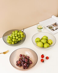 Fresh green pears and grapes in glass bowls with scattered cherry tomatoes on minimal white table.
