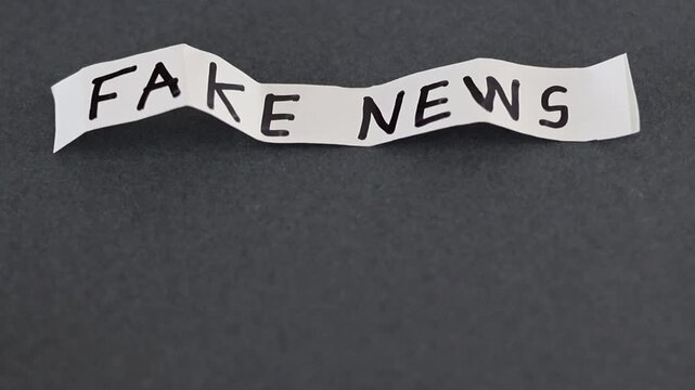 Un primer plano de un papel de color blanco con las palabras noticias falsas con movimiento en un fondo gris oscuro