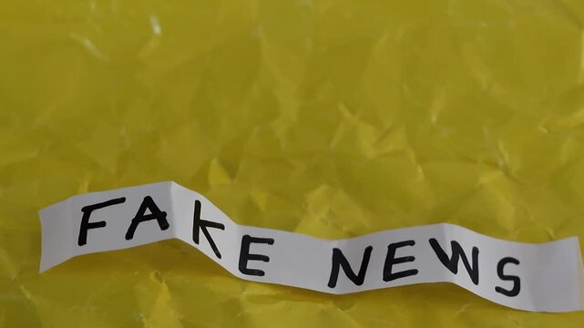 Un primer plano de un papel de color blanco con las palabras noticias falsas con en movimiento en un fondo amarillo