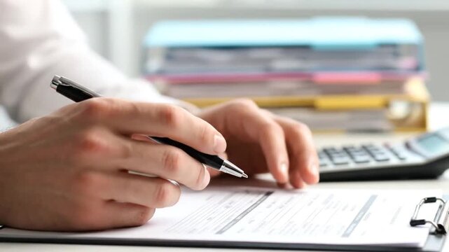 Close Up of Person Filling Out Document on Clipboard with Calculator and File Folders on Desk in Bright Office Ambiance Analyzing Data or Completing Application Forms Paperwork