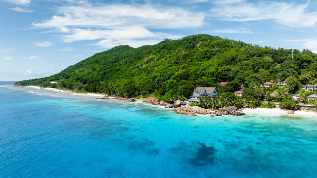 Panoramic view showcasing lush green hills descending into turquoise waters of the coastline under a clear sky. Anse Patates. Seychelles, La Digue. - Powered by Adobe