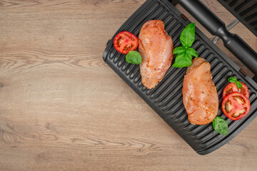 Raw marinated chicken breasts with tomatoes and basil on electric grill, top view, cooking preparation concept