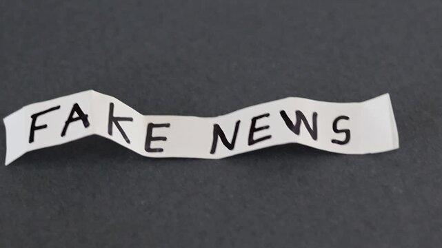Un primer plano de un papel de color blanco con las palabras noticias falsas con movimiento en un fondo gris oscuro