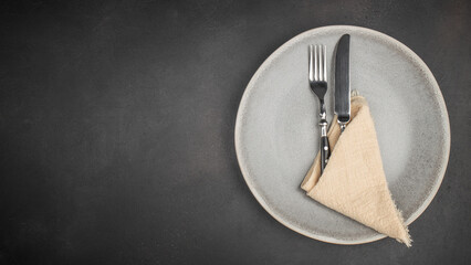 Elegant table setting with fork and knife on ceramic plate over dark textured background, top view with copy space