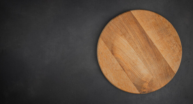 Round wooden cutting board on dark textured background, top view with copy space