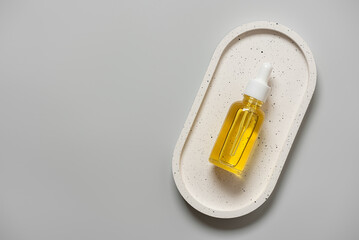 Cosmetic serum in a dropper bottle flat lay on a ceramic tray on a gray background, top view, copy space.