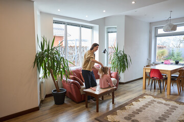 Mother brushing daughter's hair in cozy modern living room with large windows and indoor plants