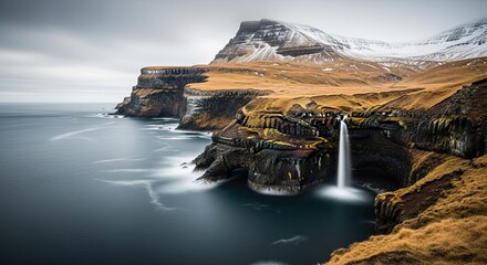 Dramatic long exposure landscape of a powerful waterfall cascading from a rugged coastal cliff into the ocean, with a majestic snow-covered mountain in the background