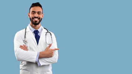 A friendly doctor wearing a white coat and tie stands confidently with a stethoscope around his neck. He is smiling and pointing towards the right side of the scene. © Prostock-studio