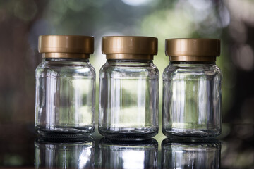 Three clear glass jars with gold lids. Empty sample jars arranged in a row on nature background