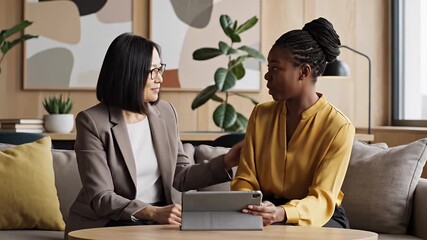 Professional diverse businesswomen discuss strategy in a modern office lounge Collaborating with a digital tablet they focus on communication and teamwork - Powered by Adobe