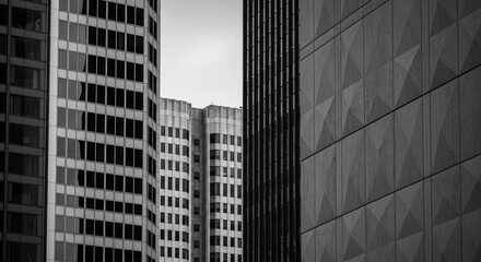 A dramatic black and white architectural abstract of modern skyscraper facades with geometric patterns, contrasting textures, and repeating windows in a dense urban financial district