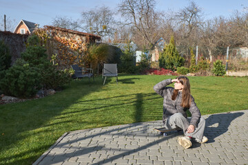Young woman relaxing on skateboard in sunlit garden setting