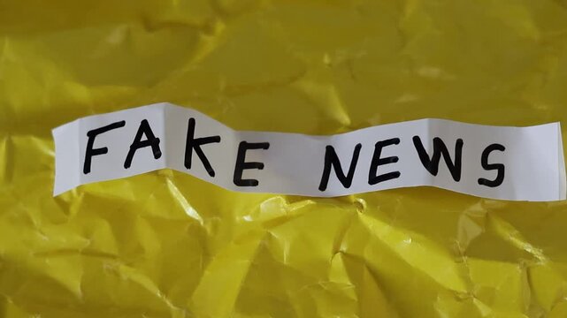 Un primer plano de un papel de color blanco con las palabras noticias falsas con en movimiento en un fondo amarillo