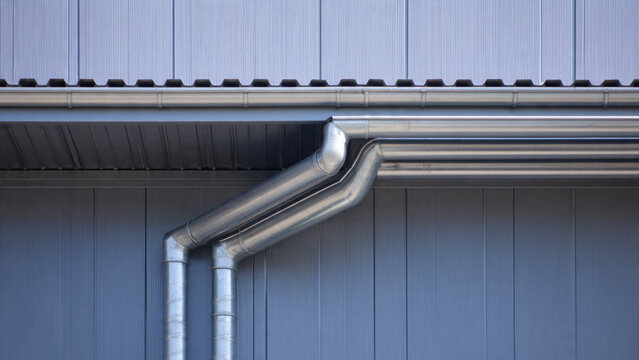 Close-up of a modern building's silver metallic gutter and downspout system, effectively managing rainwater from the roof.