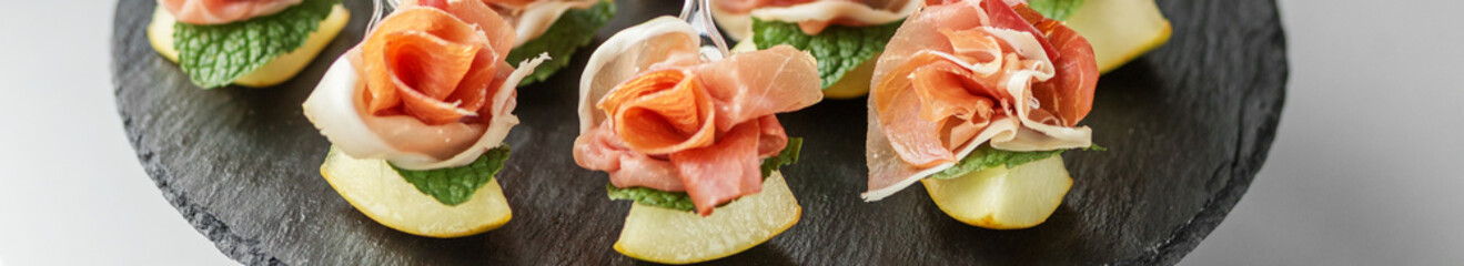 Prosciutto and pear appetizers with mint on slate. Banner for website