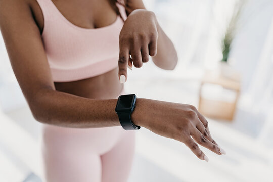 A young black woman in comfortable workout attire points at her fitness tracker while taking a breather. She checks her heart rate and calories burned, highlighting modern workout tools. - Powered by Adobe