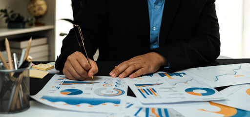 A business professional engaged in a detailed analysis of financial reports and graphs at a modern office desk, showcasing focus and commitment to data-driven decisions.Noogenesis