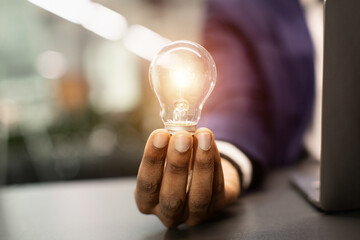 Unrecognizable black businessman with illuminated light bulb, working on laptop at office, cropped, concept for idea, innovation and inspiration in business, business opportunities, copy space