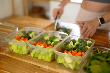 Closeup of a woman hand placing freshly cut fruits and vegetables into food storage containers, meal prep, and food preservation