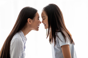 Naklejka premium A loving interaction takes place between a young woman and her daughter as they touch noses. Both are smiling, showcasing their strong bond and happiness against a white background.