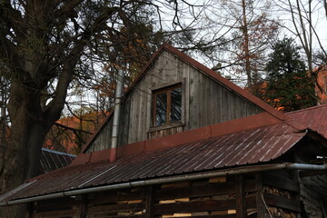 A rustic, weathered wooden shed or barn with a rusty red tin roof, used as a woodshed to store firewood. This image evokes rural life, autumn, and preparing for winter in the countryside.